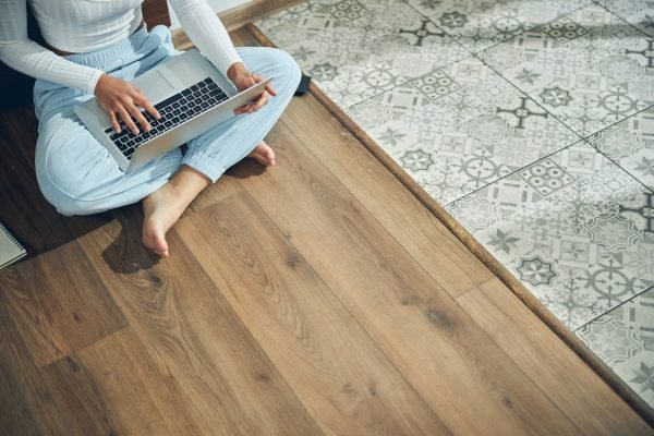 Top view of a barefoot female freelancer sitting with her computer on the kitchen floor